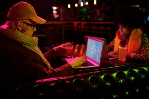 Two people coding on their laptops in a booth